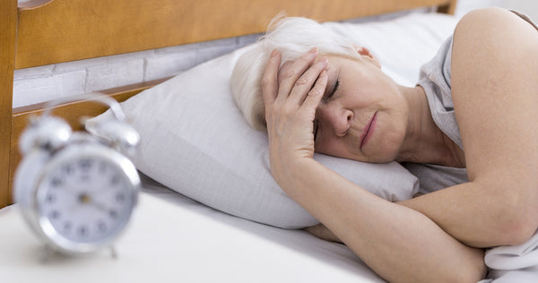 mature woman lying down in bed holding head