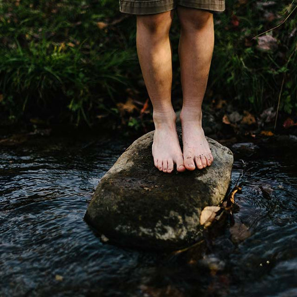 Child's bare feet on a rock amidst water by Jordan Whitt