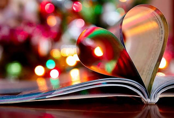 Book pages curled in the shape of a heart and reflecting festive Christmas lights