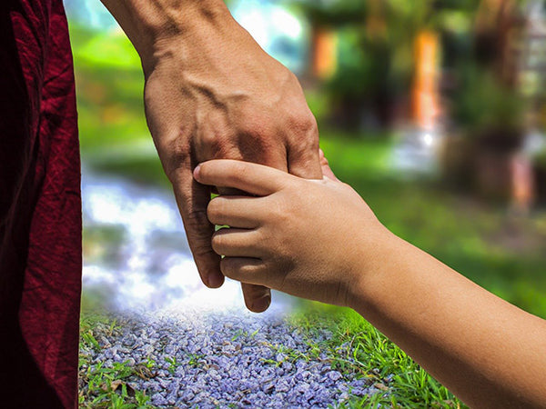 A child's hand holding adults with nature in the foreground