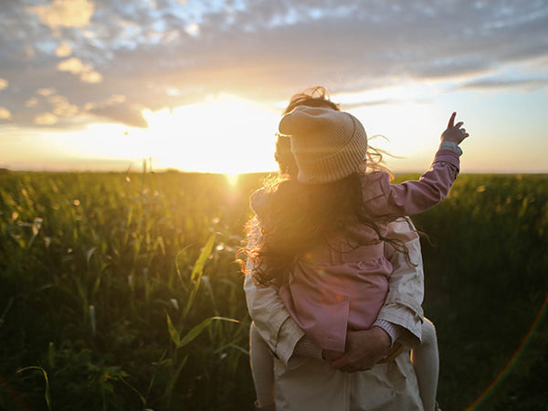 Mother and daughter enjoying sunset before a grassy field