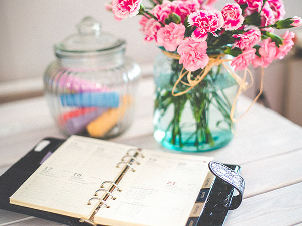  An open planner laying on a table with a vase of flowers