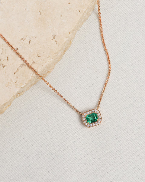 Petite emerald cut gemstone pendant crafted in rose gold, on white background with travertine.