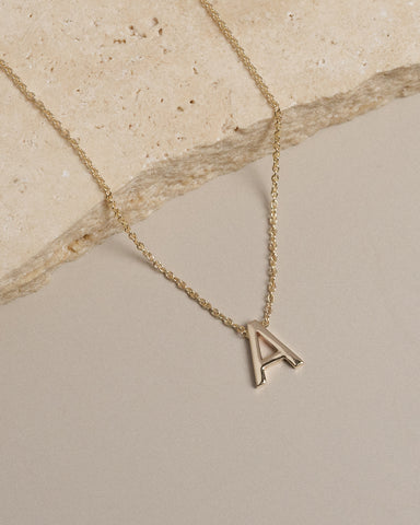 Close up image of a petite A initial necklace crafted in yellow gold.