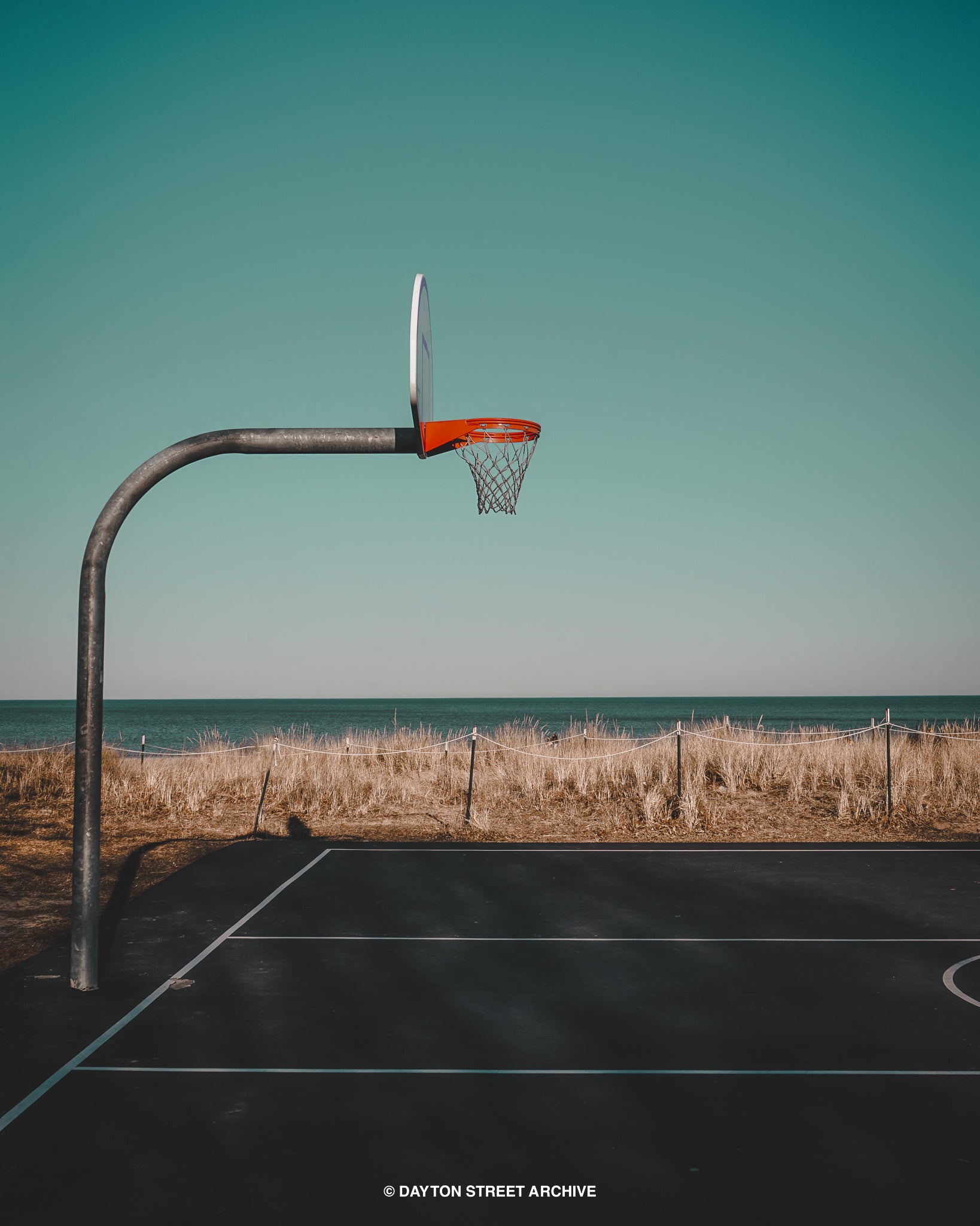 photograph of basketball hoop on beach with smooth sky background