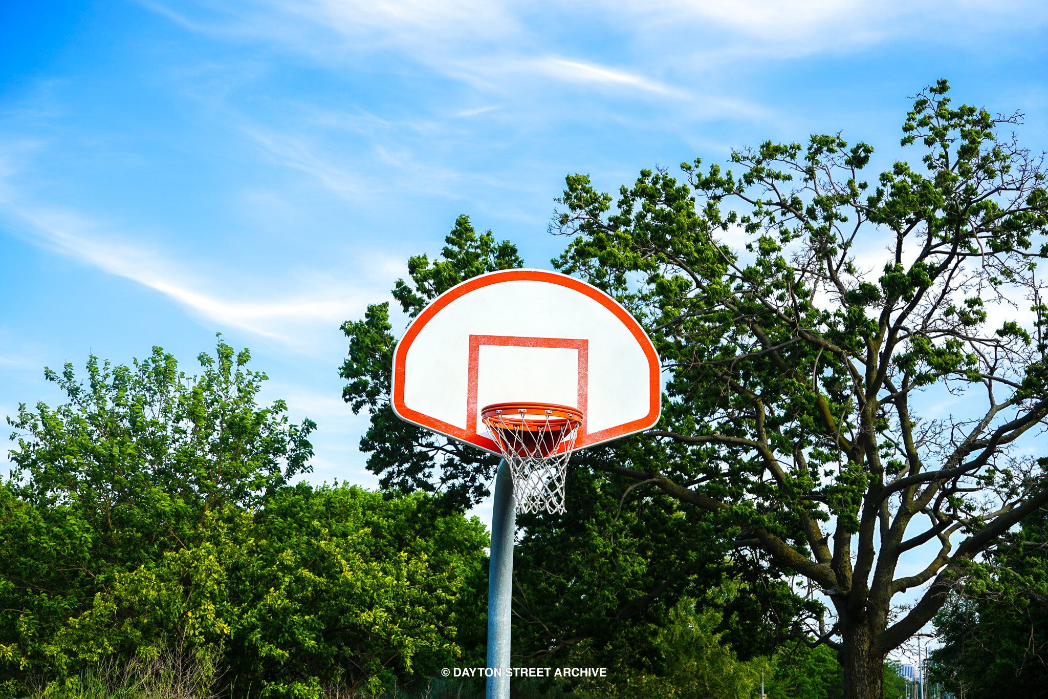 beautiful basketball hoop with trees and smooth cloudy blue sky in background