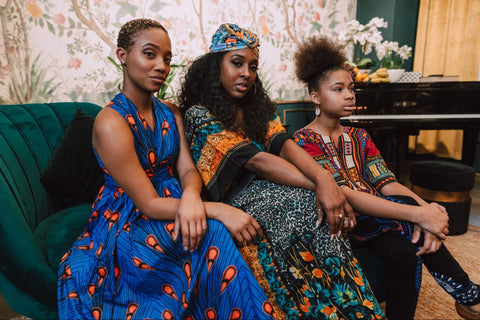 Three women sitting together wearing colorful outfits.