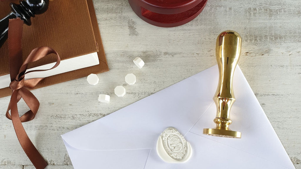gold brass wax seal stamp and white wax seal on envelope with sealing wax beads scattered