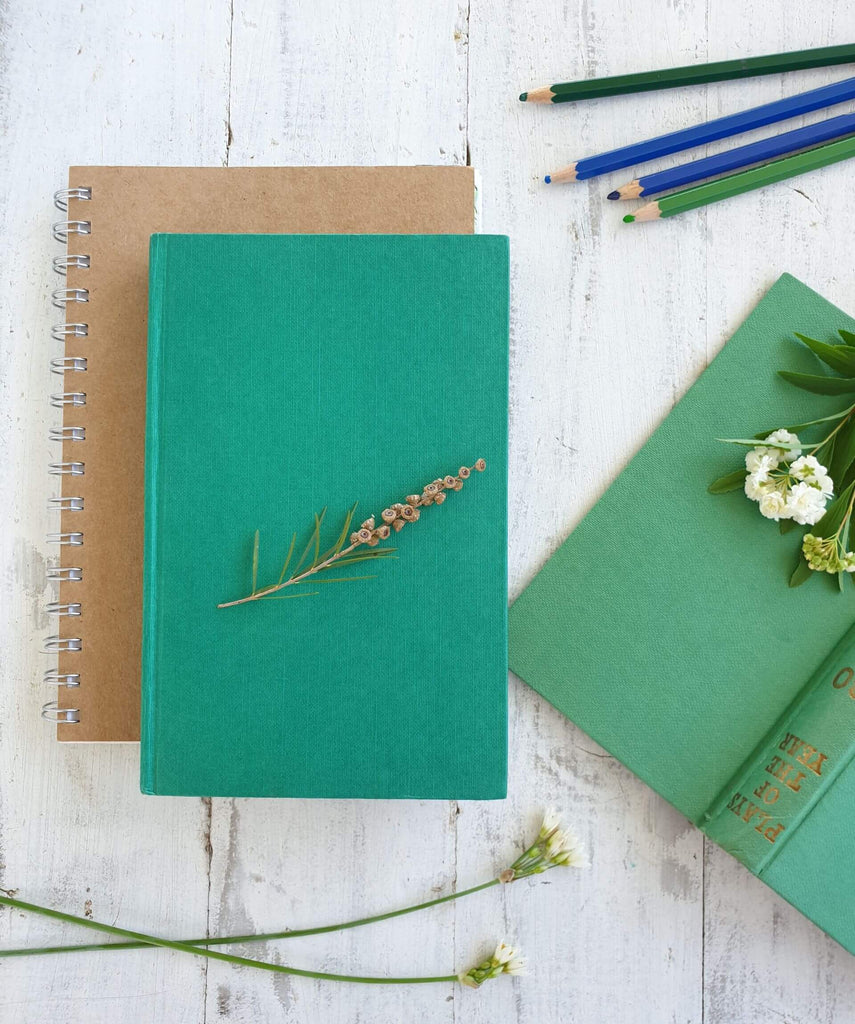 green journal and brown notebook with vintage book and pencils