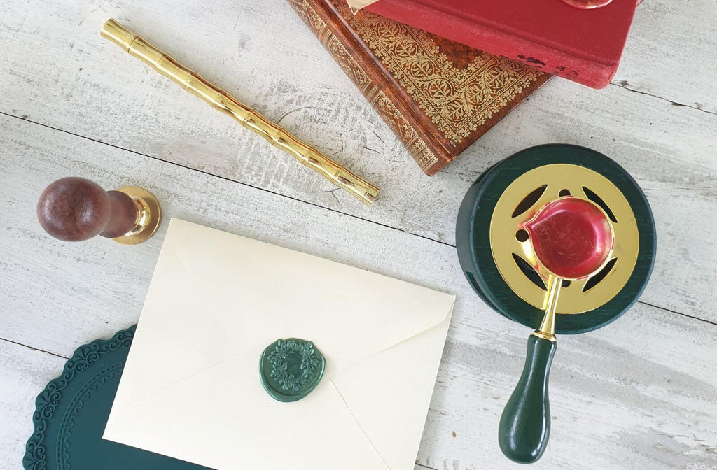 green wax seal on envelope with wax seal stamp, brass pen and red sealing wax