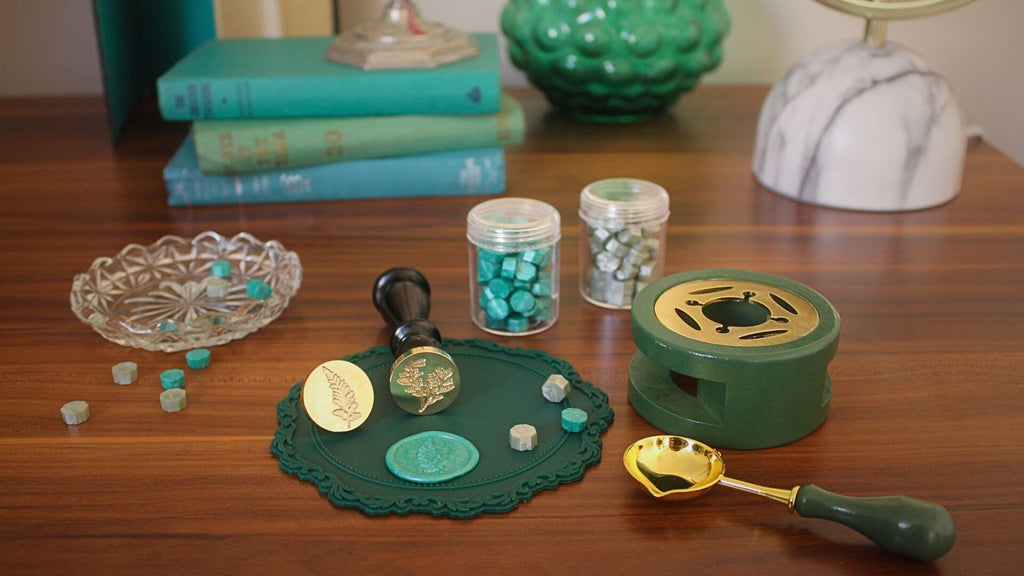 desk with green sealing wax, a wax seal stamp, wax seal mat and vintage books