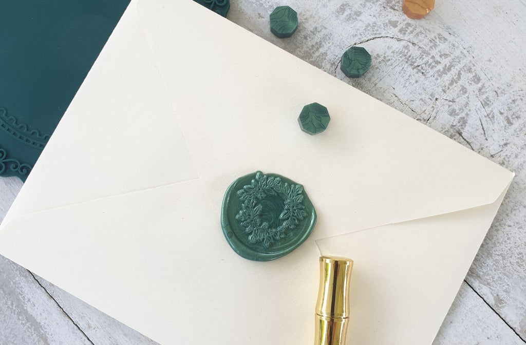 envelope sealed with wax seal featuring foliage wreath design with gold pen and sealing wax