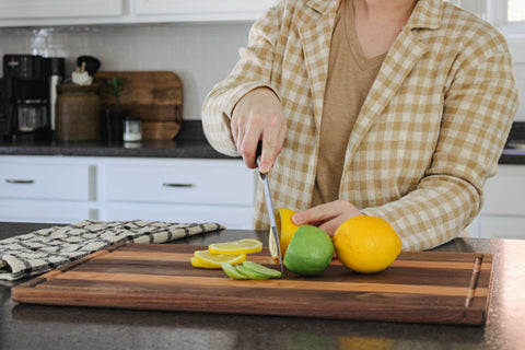 Person slicing lemons and limes on the cutting board.