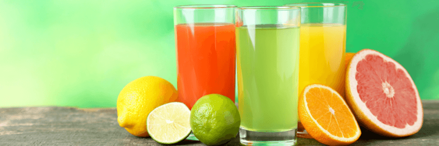 3 glasses filled with citrus fruit juice and various citrus fruit surrounding