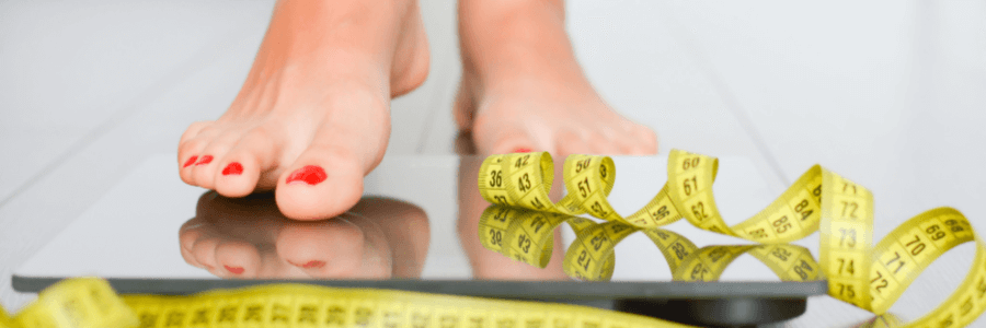 feet stepping onto body weight scale with yellow measuring tape on the floor