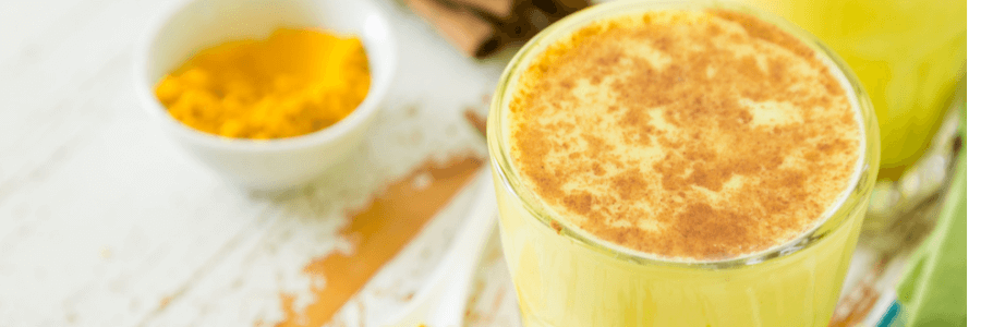 Yellow turmeric latte in glass cup with cinnamon sprinkled on top