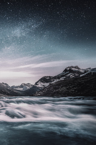 Starry sky above mountains with waves breaking on shore beneath