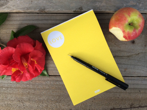 Desk with a notepad, pen, apple and a flower on it