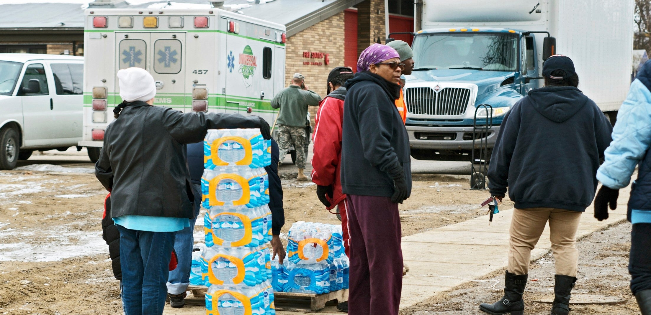 Photo of People distributing bottled water, and ambulance and a box truck are in the background