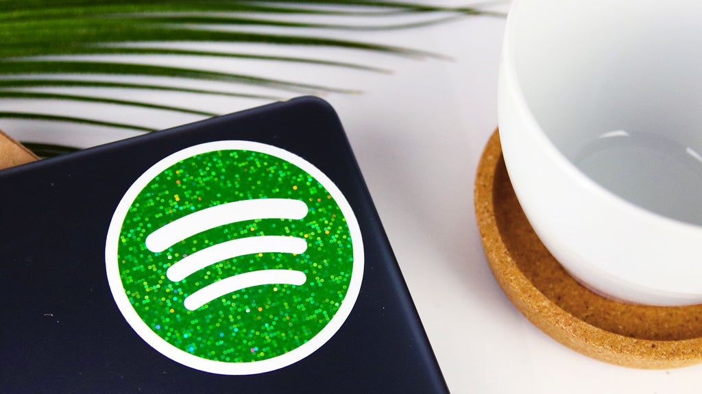 Kreisförmiger Glitzeraufkleber mit grünem Spotify-Logo auf einem Laptop