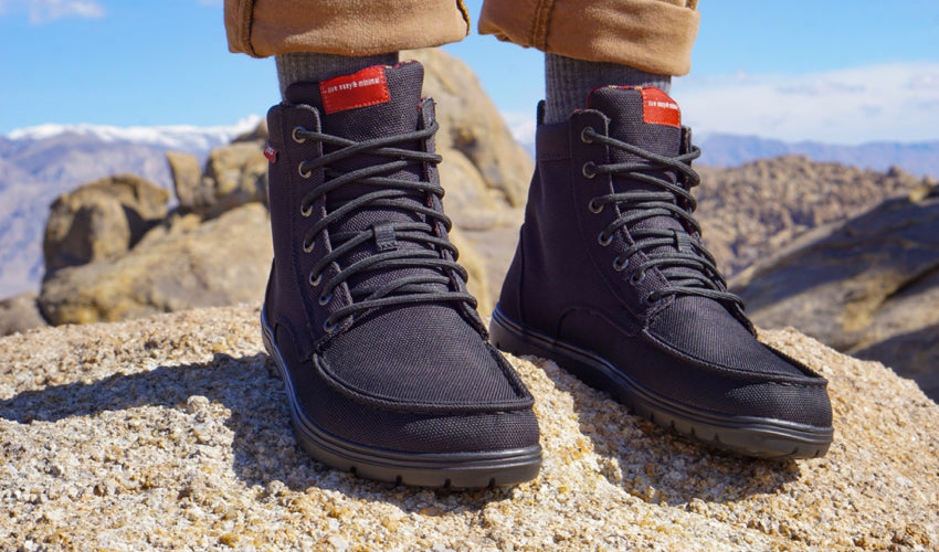 The feet and lower legs of a hiker wearing Lems Boulder Boots in Black with a mountain range in the background