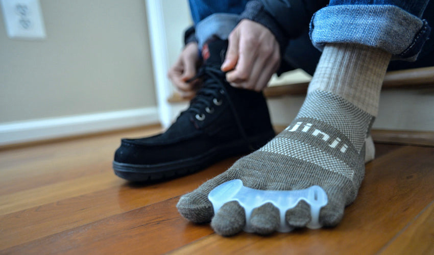 Person, with Correct Toes toe spacers and Injinji toe socks on, sitting on a stair-step and donning a pair of Black Lems Boulder Boots