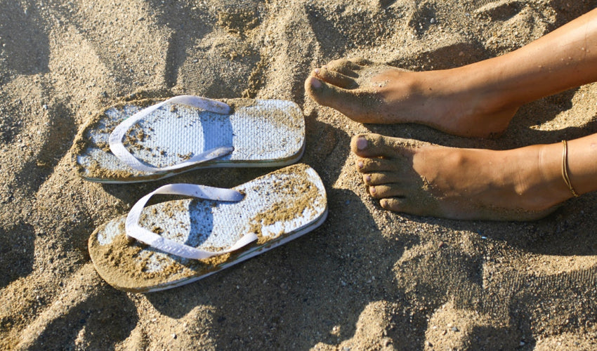 Top down view of a pair of bare feet and flip-flops at the beach