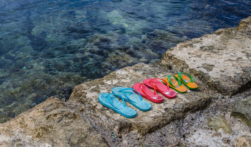 Several pairs of flip-flops sitting side by side on a stone wall overlooking water