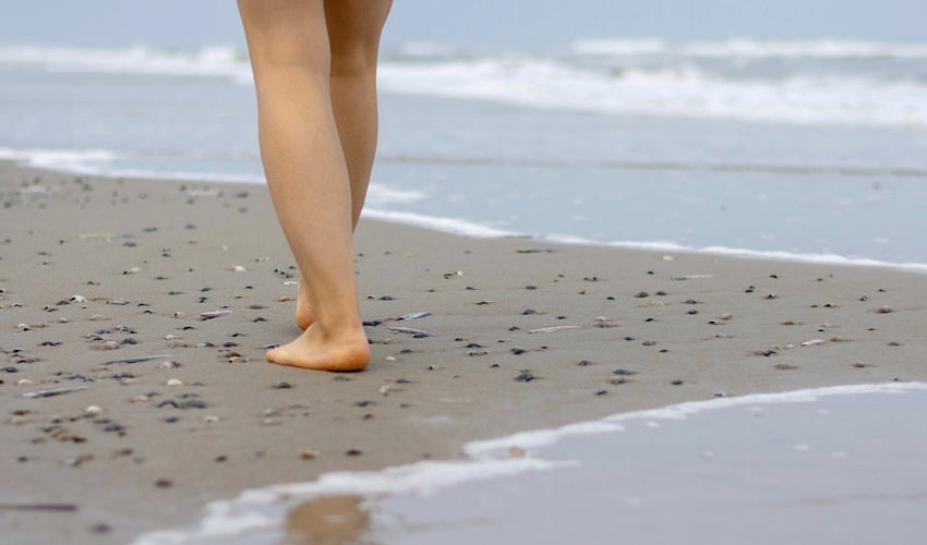 Woman walking barefoot among seashells on a beach