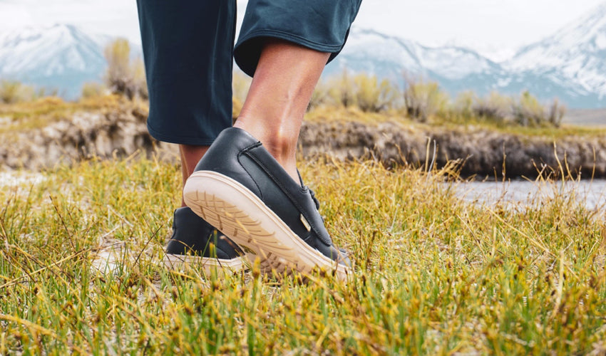 A person standing in a grassy meadow and wearing Lems Mariner Navy boat shoes