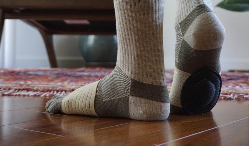 A person standing on a wood floor and wearing Injinji toe socks and Strutz Rx foot pads