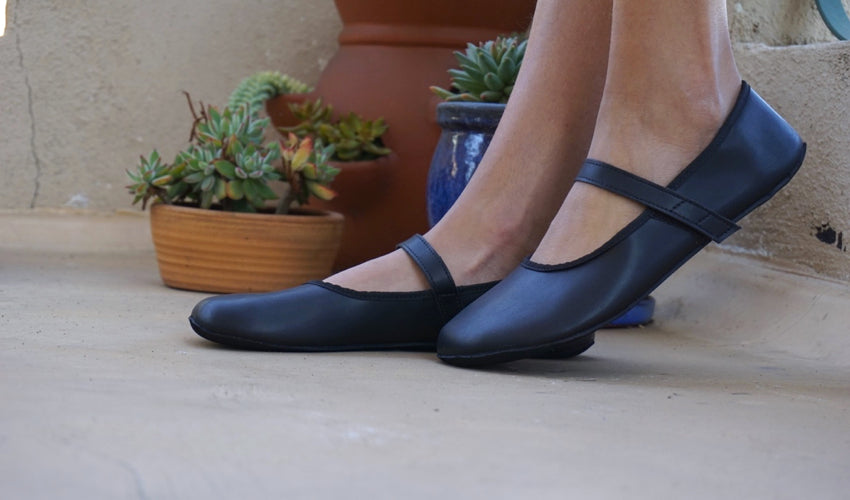 A side view of a pair of Ahinsa Ananda Ballerina shoes in Black with several potted plants in the background