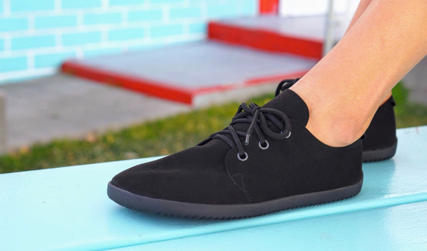 Person seated on a picnic table and wearing a pair of Ahinsa Bindu Bare Black casual shoes