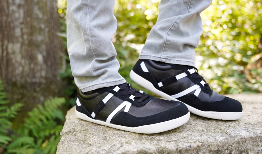 Side view of a person standing on a stone bench wearing Xero Kelso Black/White shoes