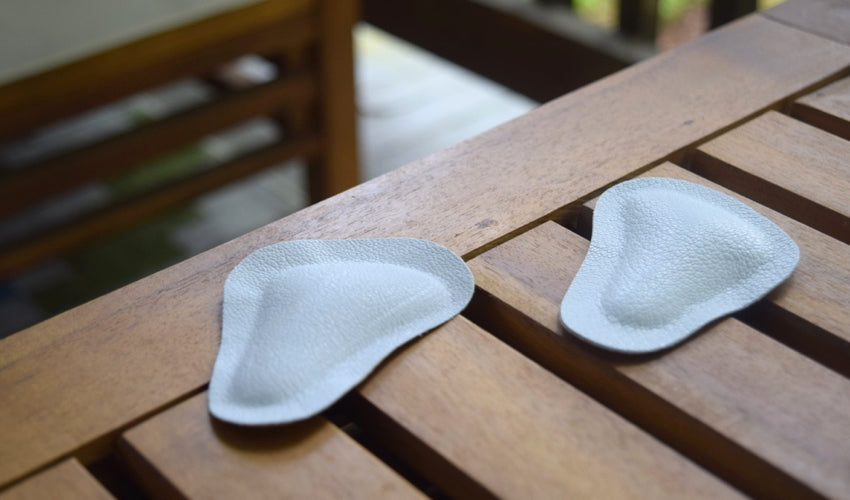 A pair of Pedag metatarsal pads sitting on top of a slatted wood outdoor coffee table