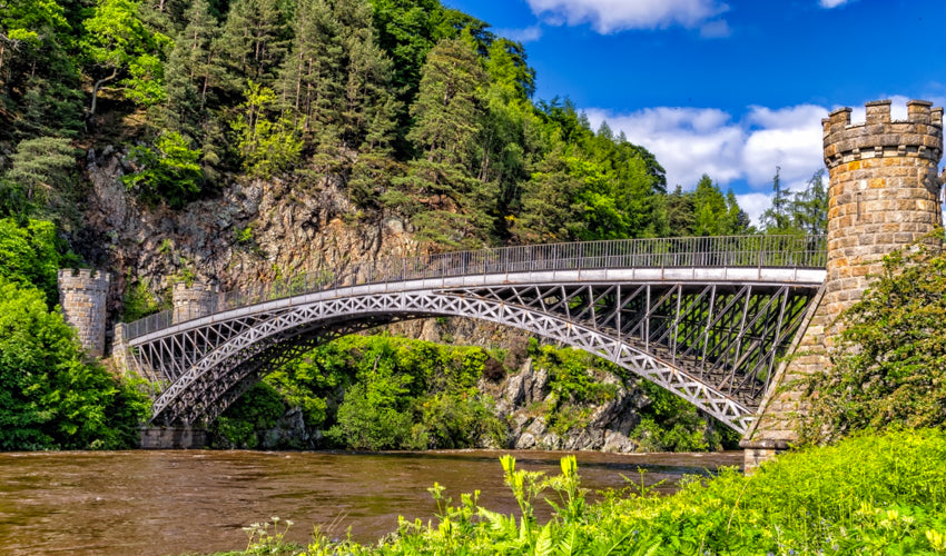 An arch bridge spanning a river with a hill and forest in the background