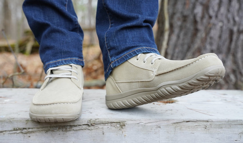 A person standing on top of a wooden bench wearing Lems Telluride Boots with the left foot popped up