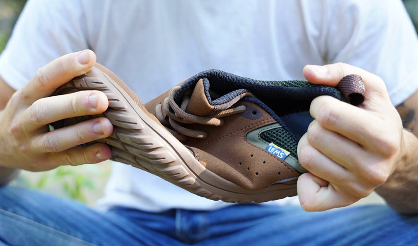 A seated person twisting a Lems Primal Zen Woodland shoe with both hands