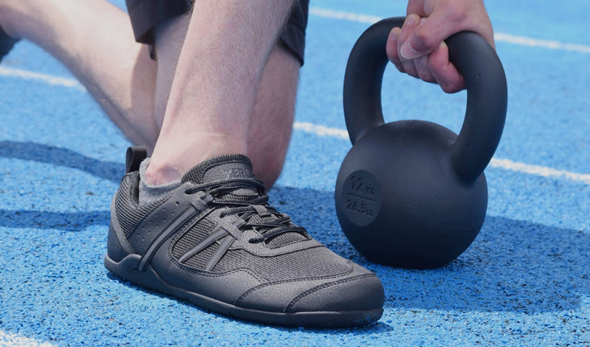 An athlete in Xero Prio Black shoes performing a lunge with a kettlebell on a running track