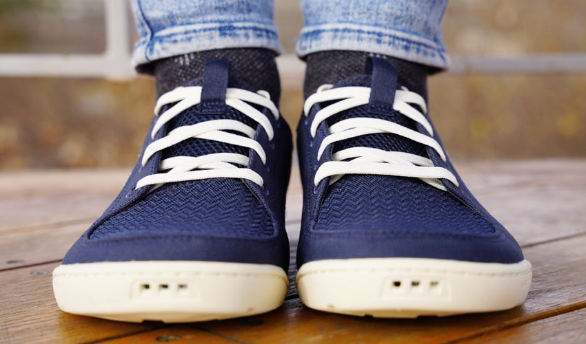 Head-on view of the side by side feet of a person wearing Navy/White Astral Loyak shoes and standing on a wood deck