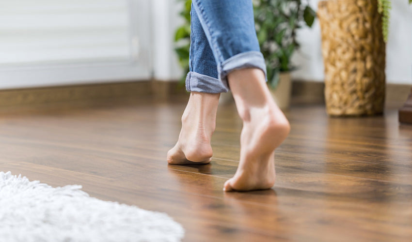 Person walking barefoot on wood floors inside a house