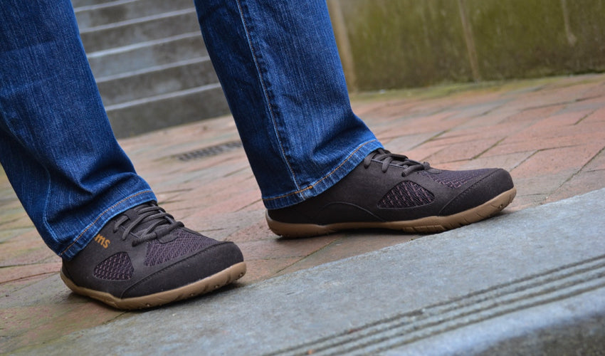 A person standing on cobblestones and wearing Lems Primal 2 Brown shoes