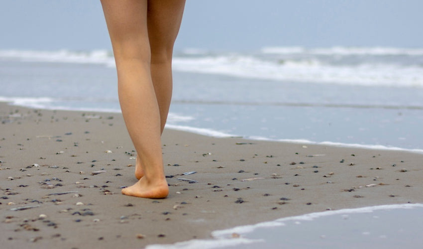 A woman walking barefoot among seashells at the beach