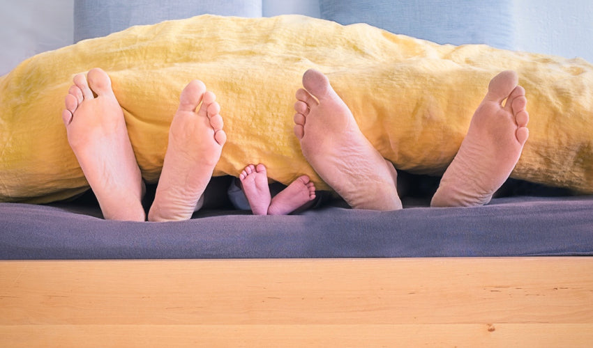 The soles of the feet of a family of three lying under a duvet