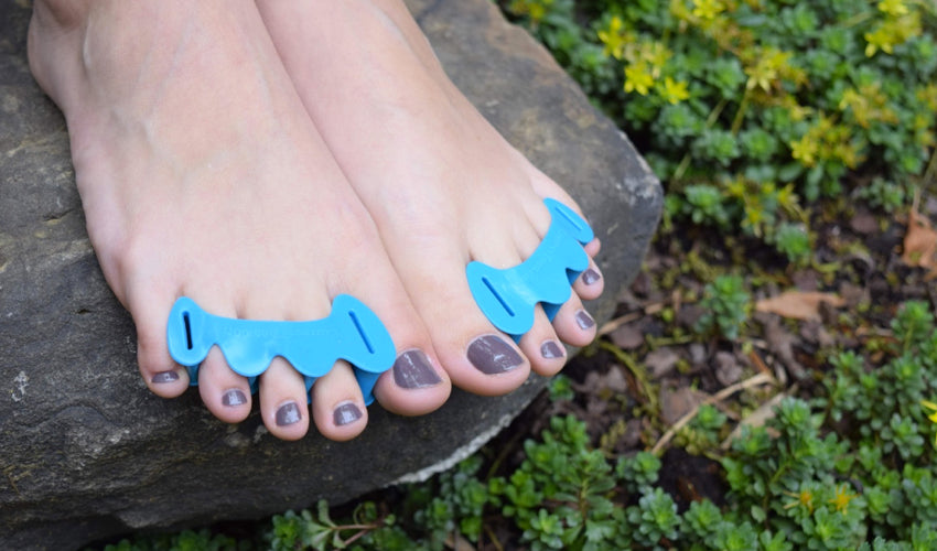 A pair of bare feet,  in a garden setting, adorned with Correct Toes Aqua toe spacers