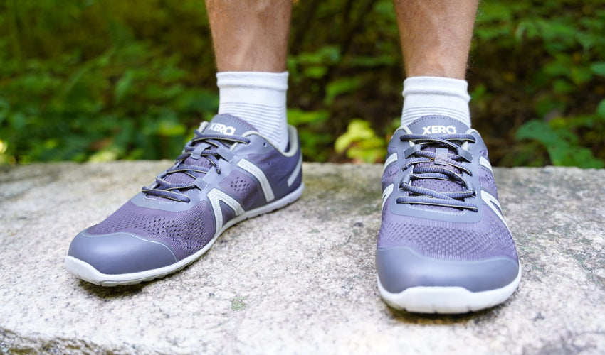 The feet and lower legs of a runner wearing Xero HFS shoes and standing on the top of a stone bench
