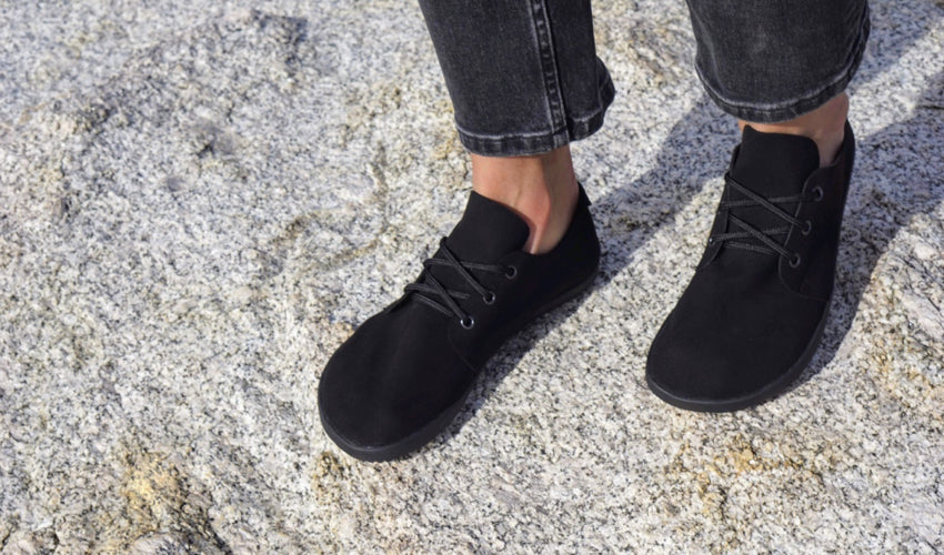 Person standing on a large stone and wearing Ahinsa Bindu Bare Black casual shoes