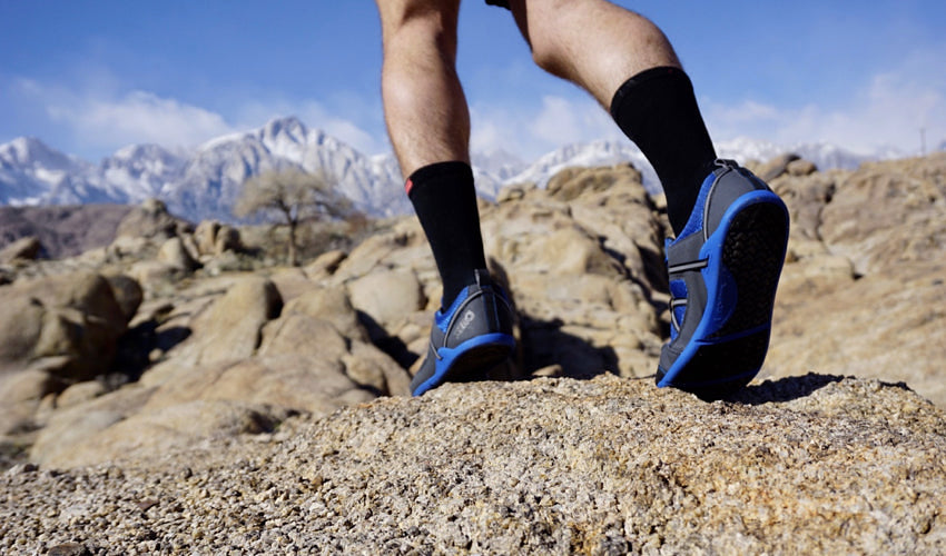 An athlete wearing Xero Prio athletic shoes and running toward a group of snowy mountains