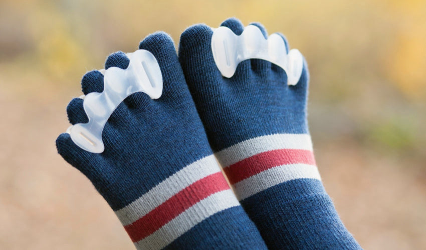 A close-up shot of a person wearing Correct Toes toe spacers and Injinji toe socks with fall colors in the background