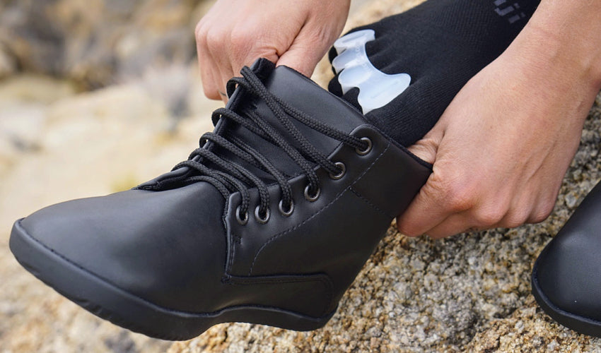 A hiker wearing Correct Toes toe spacers while putting on Ahinsa Trek Bare Ankle boots